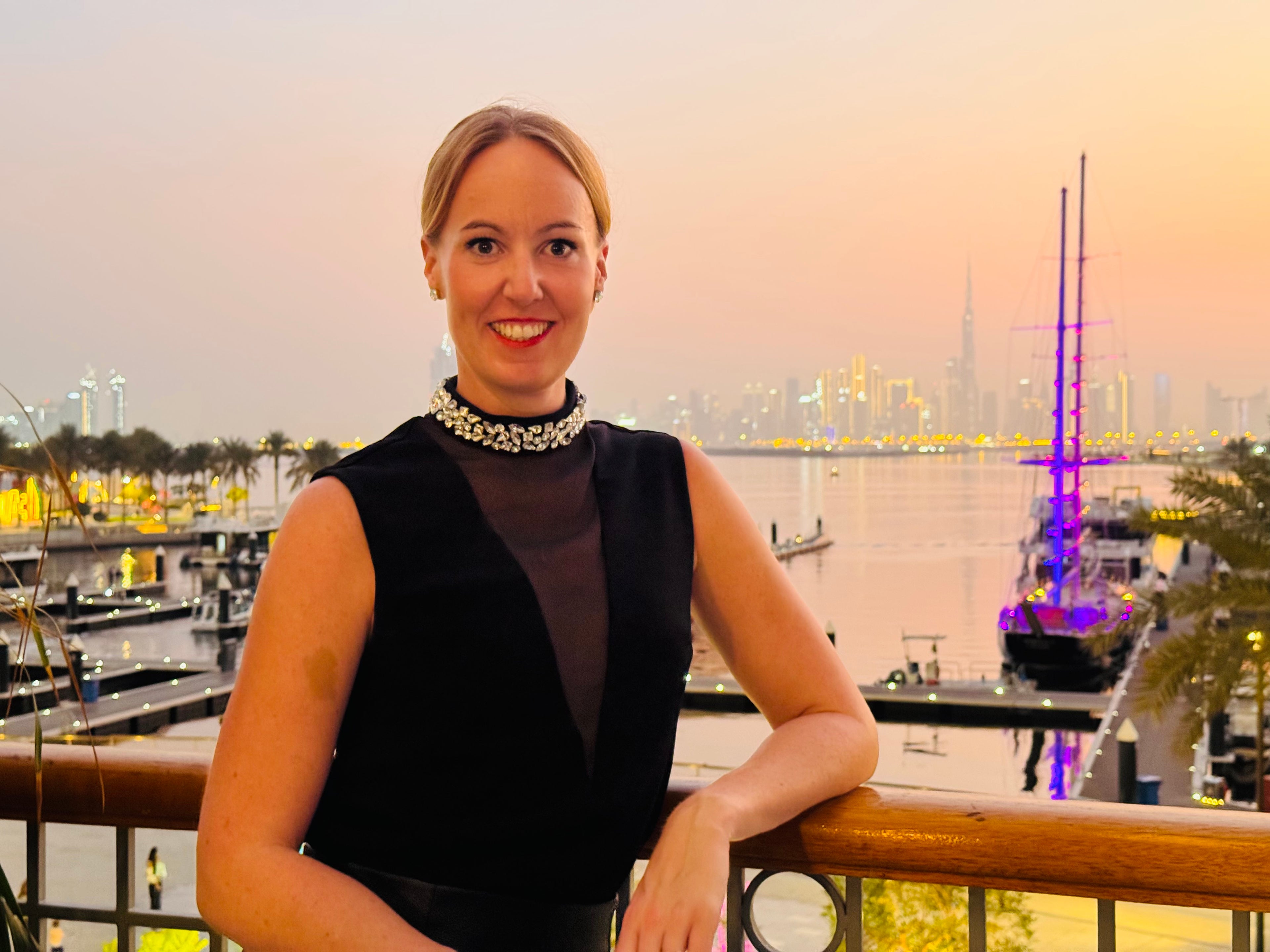Carina Schäfer im schwarzen Kleid und edler kristallkette um den hals mit der Skyline von Dubai im Hintergrund.