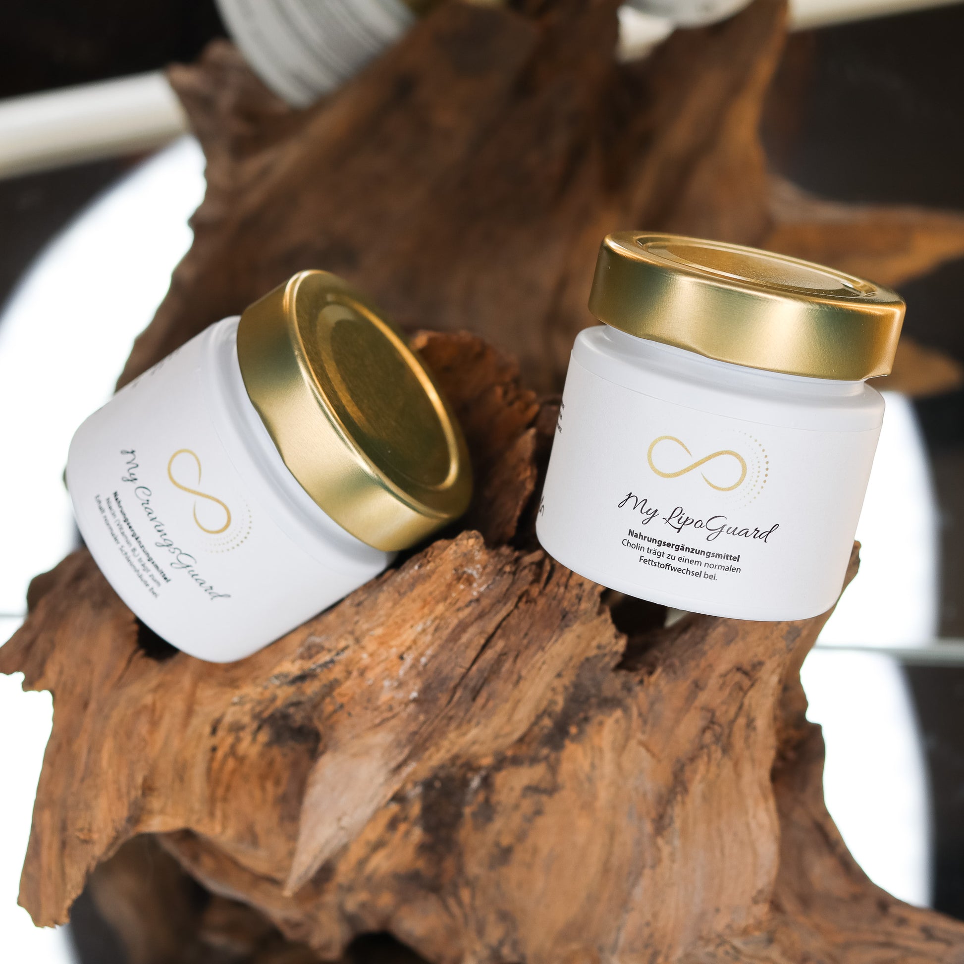 Produktbild zweier Nahrungsergänzungsmittel im weißen Glas mit goldenem Deckel, dekorativ auf einem Naturholz-Element arrangiert. Sichtbar sind die Produkte „My GravingsGuard“ und „My LipoGuard“ aus der ANS Nutrivity Secrets Serie. Das Bild dient der hochwertigen Visualisierung der Verpackung. Alle Angaben zu Inhaltsstoffen und Anwendung befinden sich in der jeweiligen Produktbeschreibung im Shop.