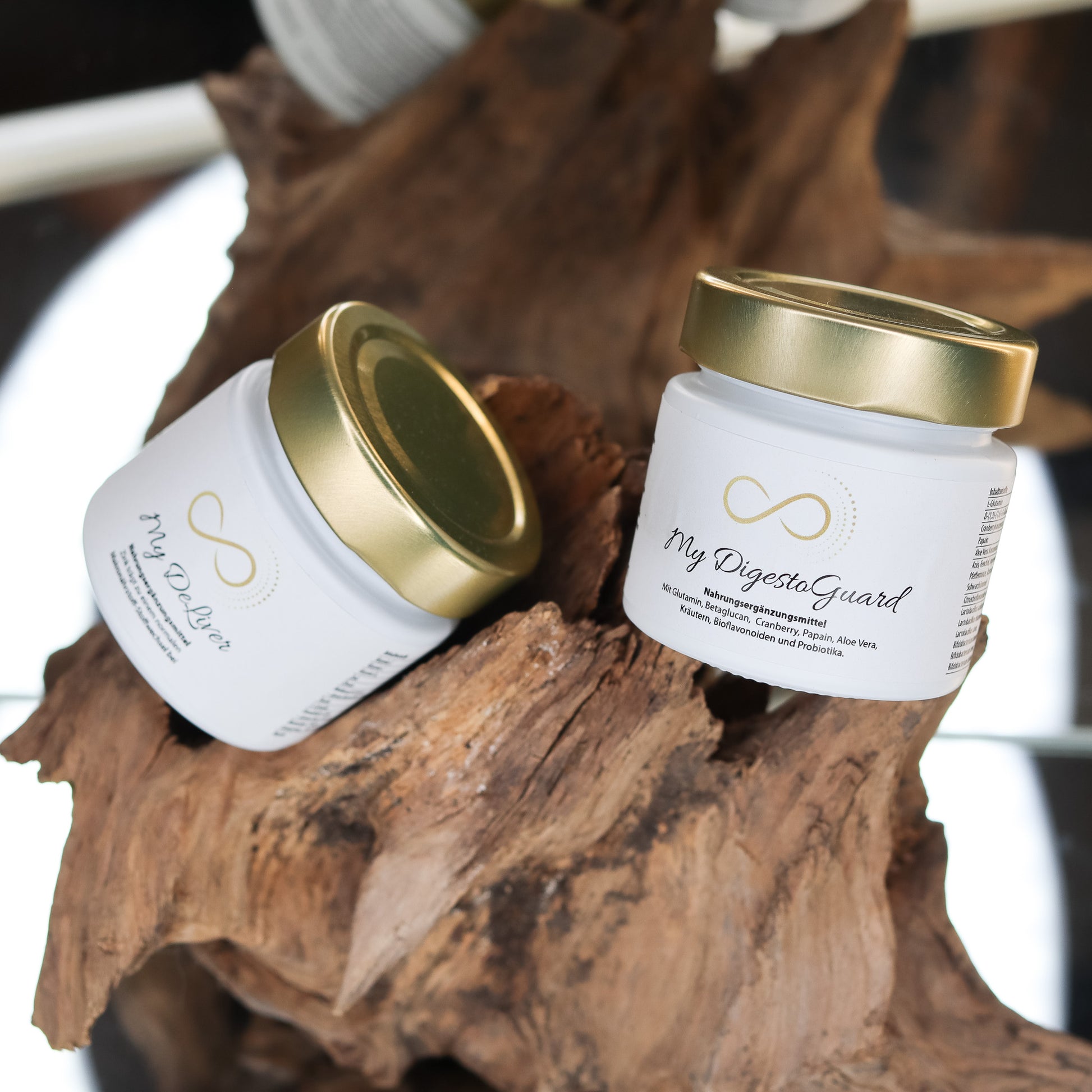 Produktbild zweier Nahrungsergänzungsmittel im weißen Glas mit goldenem Deckel, dekorativ auf einem Naturholz-Element arrangiert. Sichtbar sind die Produkte „My DeLiver“ und „My DigestoGuard“ aus der ANS Nutrivity Secrets Serie. Das Bild dient der hochwertigen Visualisierung der Verpackung. Alle Angaben zu Inhaltsstoffen und Anwendung befinden sich in der jeweiligen Produktbeschreibung im Shop.