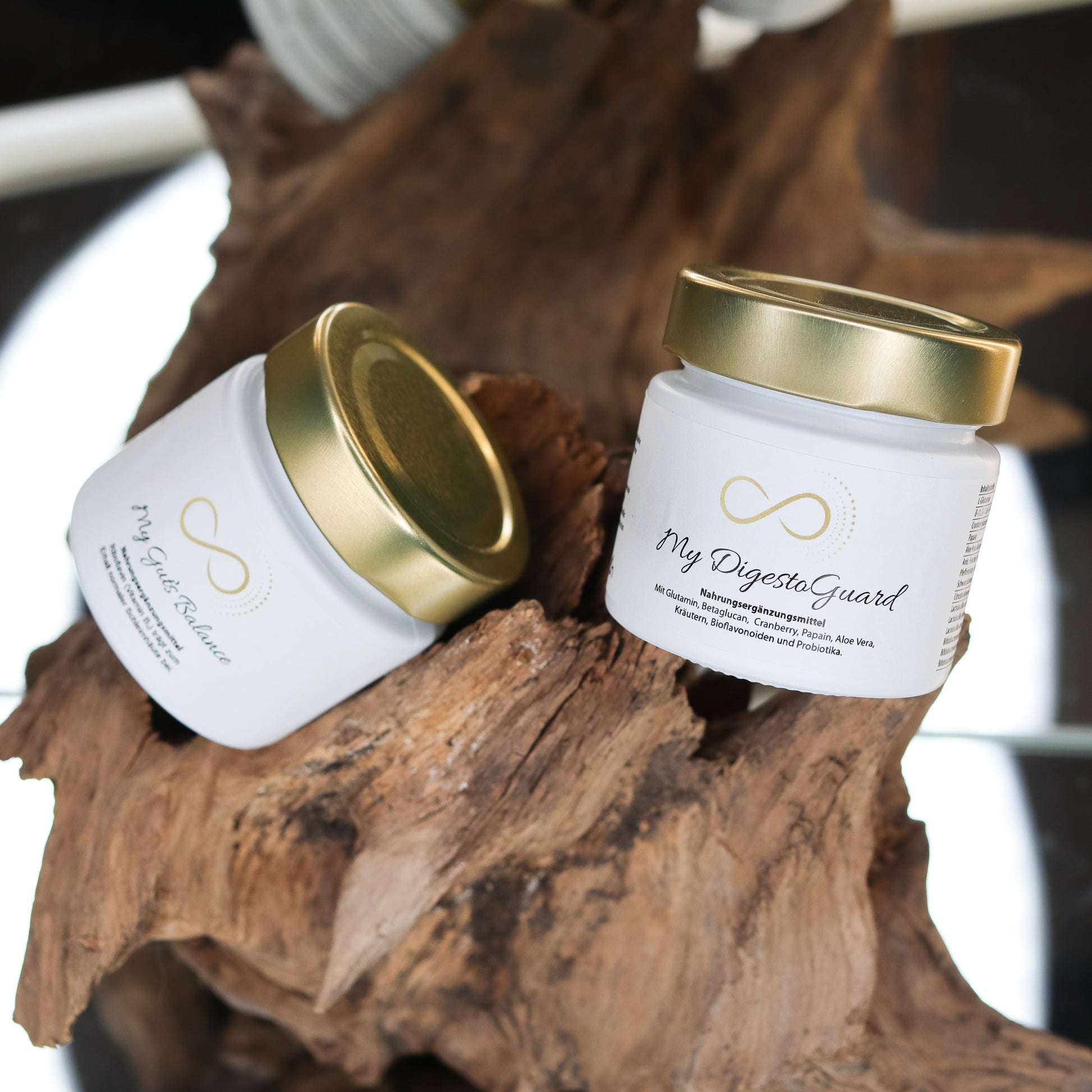 Produktbild zweier Nahrungsergänzungsmittel im weißen Glas mit goldenem Deckel, dekorativ auf einem Naturholz-Element arrangiert. Sichtbar sind die Produkte „My Guts Balance“ und „My DigestoGuard“ aus der ANS Nutrivity Secrets Serie. Das Bild dient der hochwertigen Visualisierung der Verpackung. Alle Angaben zu Inhaltsstoffen und Anwendung befinden sich in der jeweiligen Produktbeschreibung im Shop.