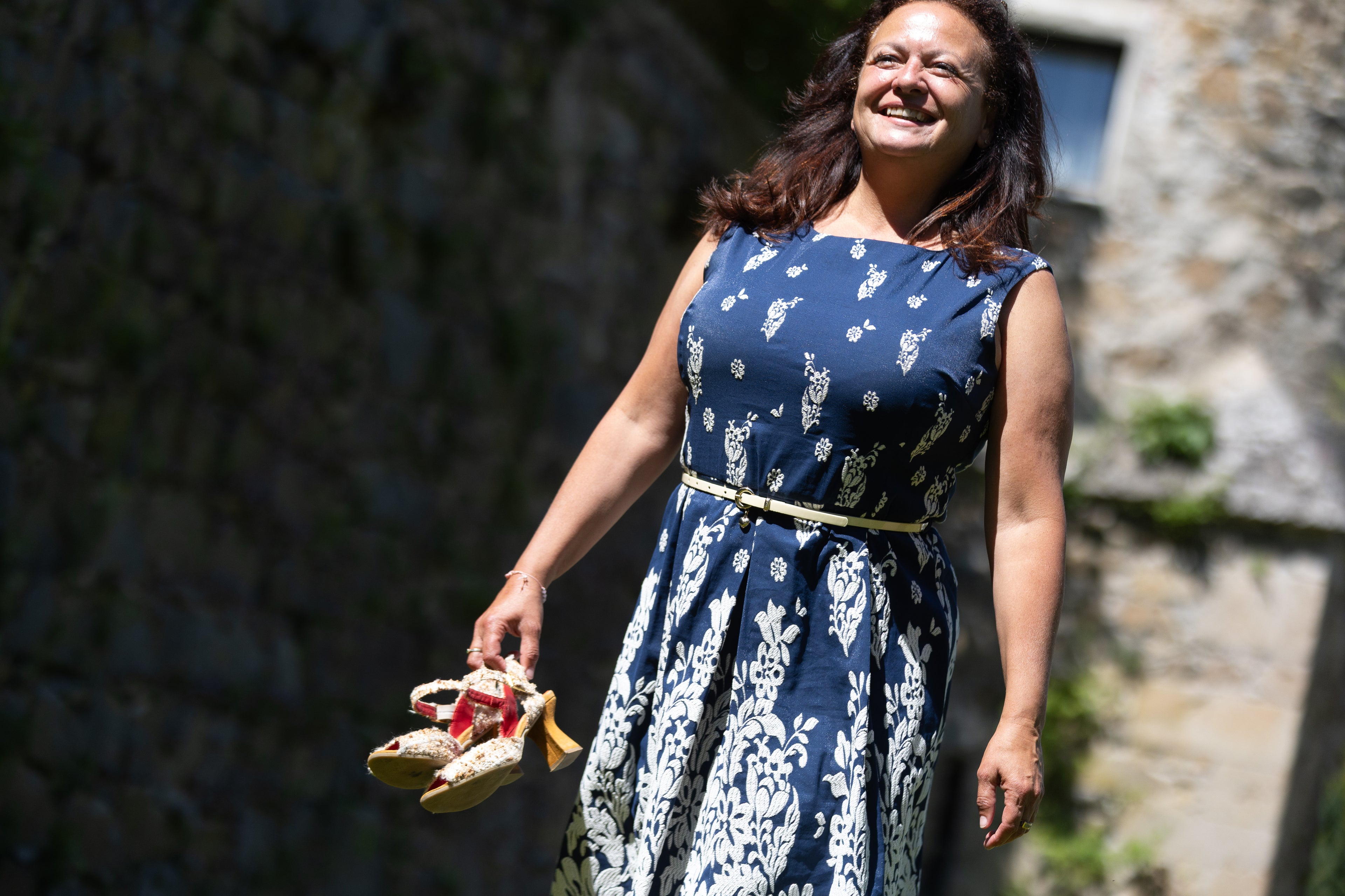Iris Reiter lachend mit Kleid und Schuhen in der Hand bei einem Shooting im Freien